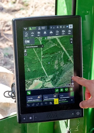 Operator's hand touching a point on a precision forestry display unit's screen, which is mounted within a green cab