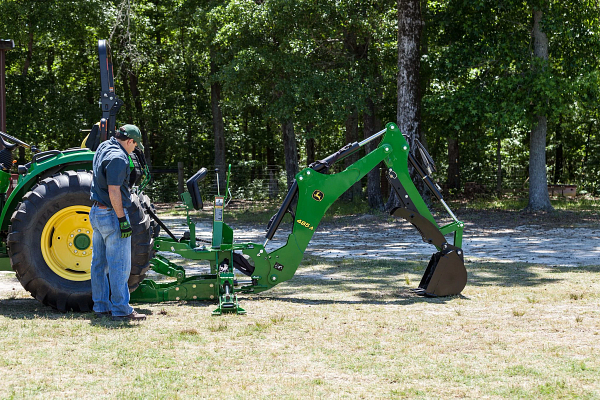 Side view of an operator standing beside a tractor's rear wheel with a 485A backhoe hookup on the back, extended and resting on grass