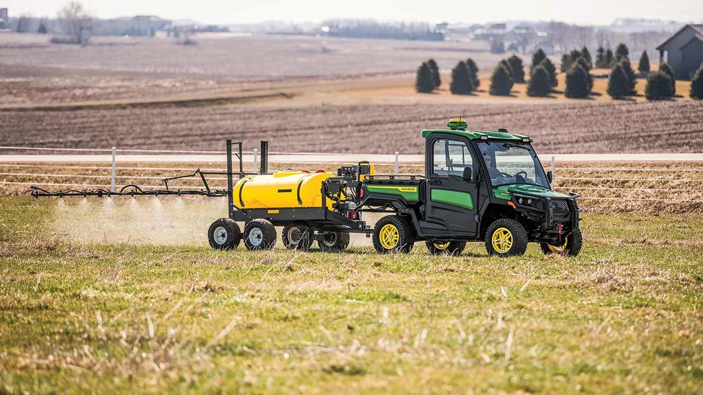 New John Deere Gator XUV 845R Signature Series Utility Vehicle with StarFire receiver moving through a field with dust swirling with a golden sunset look to the photo