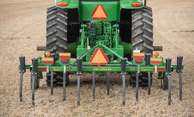 Close-up of a 610 Chisel Plow's curved black TruPosition™ standard with spring, green frame, and yellow grass in the background
