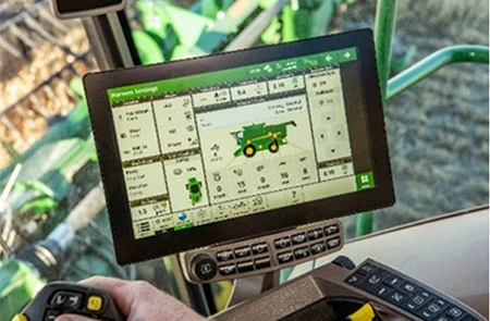 A large touchscreen display in a combine cab showing equipment settings and a graphical overview of the machine, with control buttons below the screen