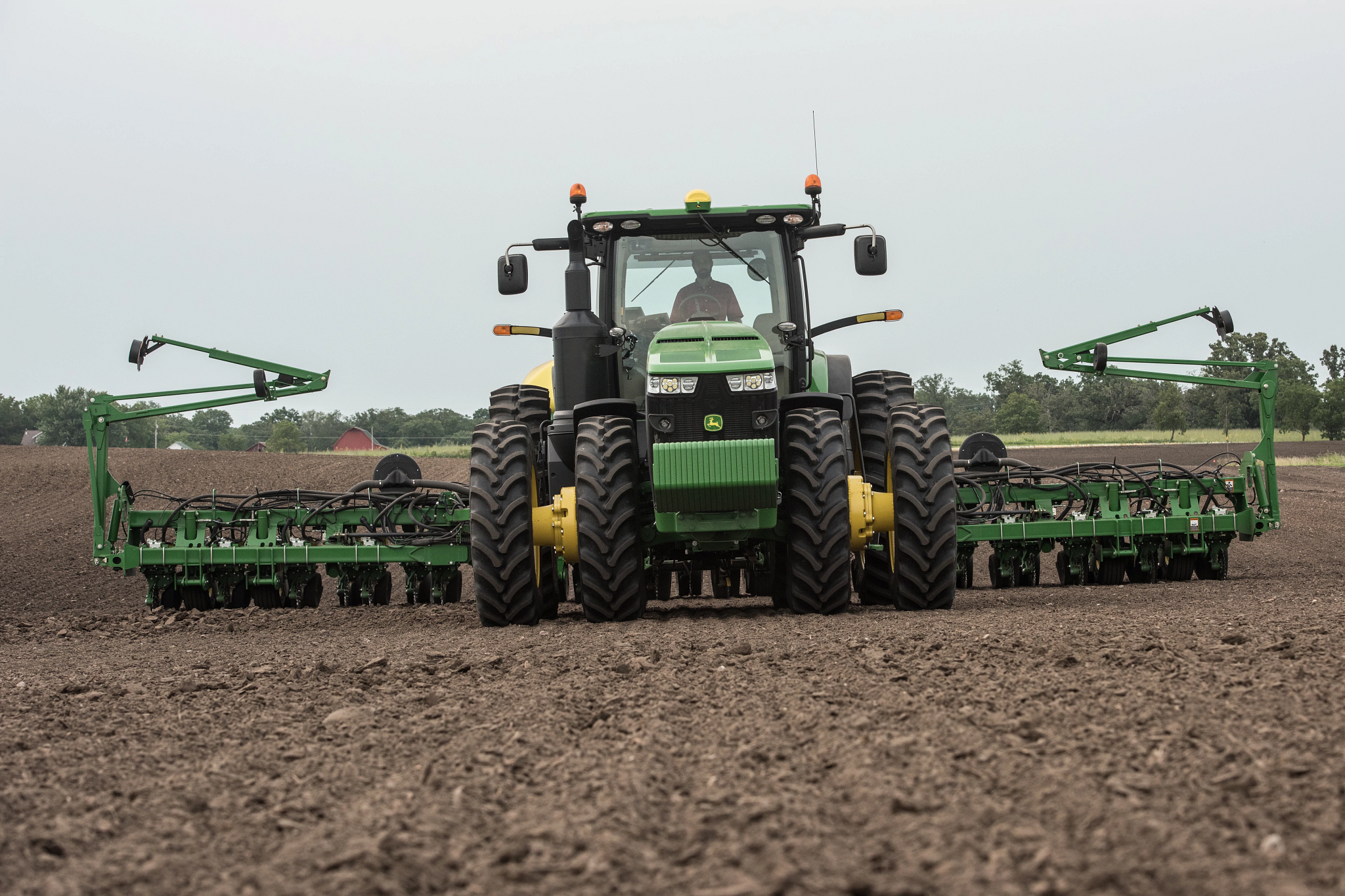Front view of an 8370R tractor with Starfire 6000 receiver atop the cab pulling a 1975 planter across brown field