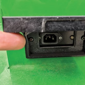 Close-up of a finger lifting the LED charge indicator on a TE Electric Gator to access IEC connector for charging.