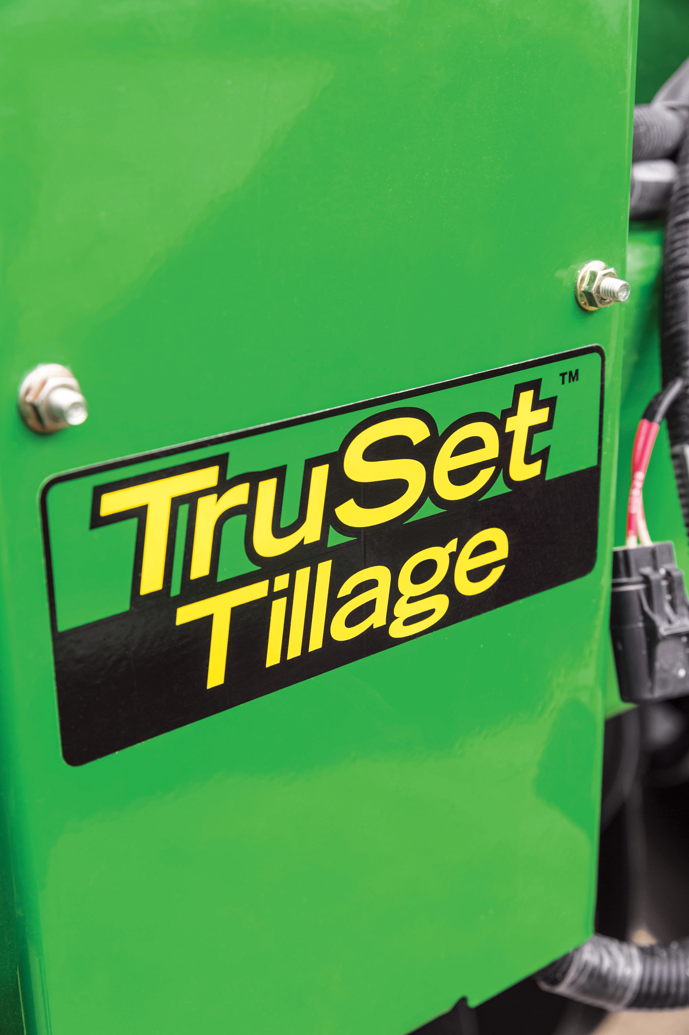 Close-up of a green agricultural machine panel displaying the “TruSet Tillage” logo, with visible mounting bolts and electrical wiring along the edge