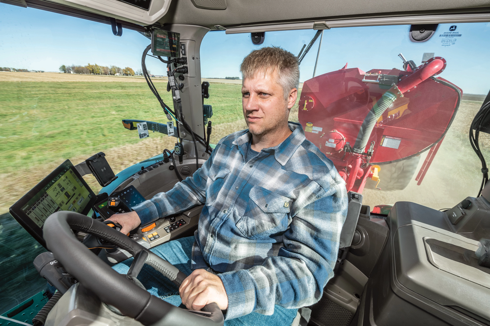 Person operating a tractor inside a cab, hands on controls with multiple screens and steering wheel visible.