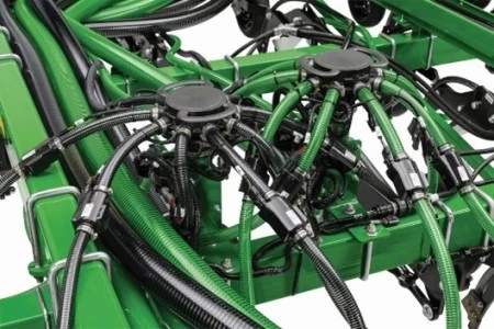 Close-up view of an air hoe drill distribution system, showing green and black hoses connected to manifold assemblies on a green metal frame