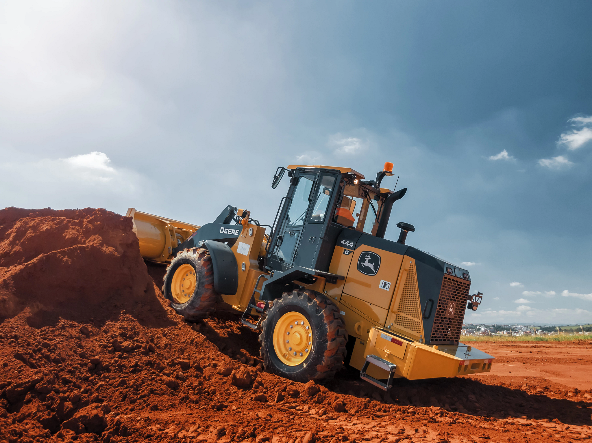 Wheel loader pushing dirt up a mound of red soil on a construction site, with the machine angled up to a cloudy sky