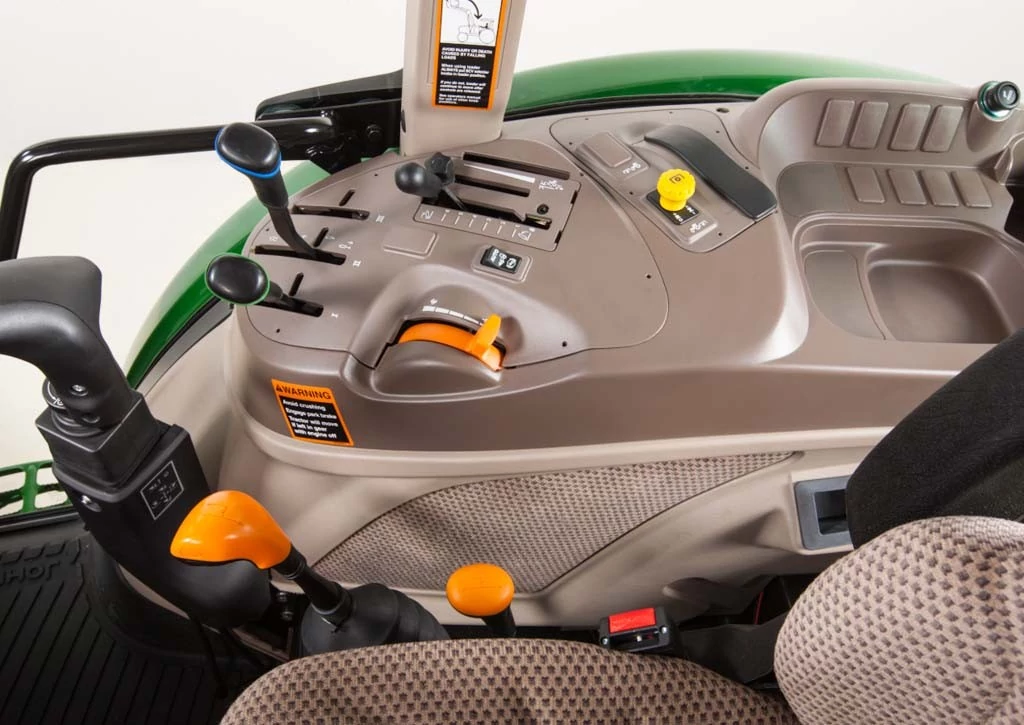 Close‑up of right‑hand control console inside John Deere tractor cab, showing hydraulic levers, throttle, PTO control, switches, cup holder, and orange adjustment handles beside the operator seat.