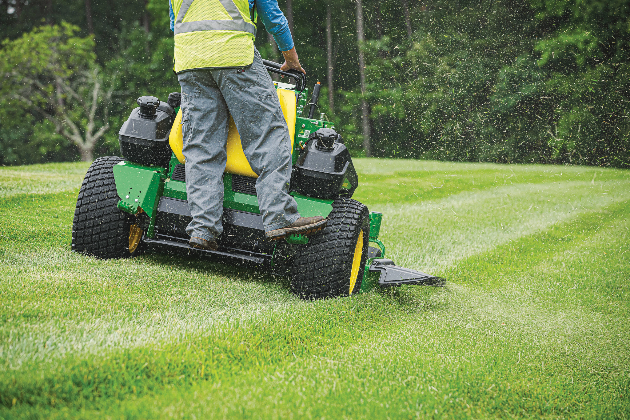 Rear view of the lower 3/4ths of a yellow-vested operator mowing a lawn with a Q850R QuikTrak Stand-On mower
