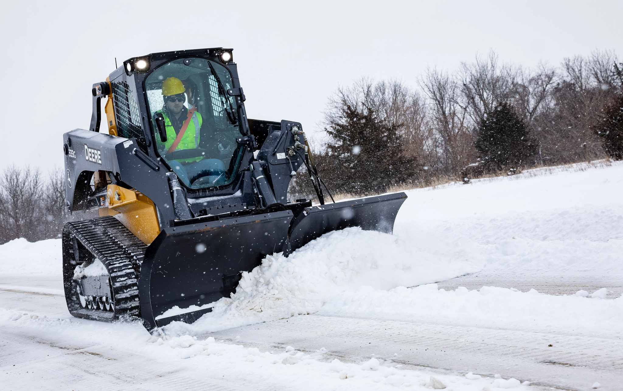 Front right view of a 333G Compact Track Loader pushing snow along a road with a BV9 V Blade attachment