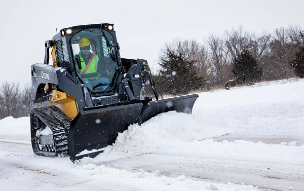 Front right view of a 333G Compact Track Loader pushing snow along a road with a BV9 V Blade attachment