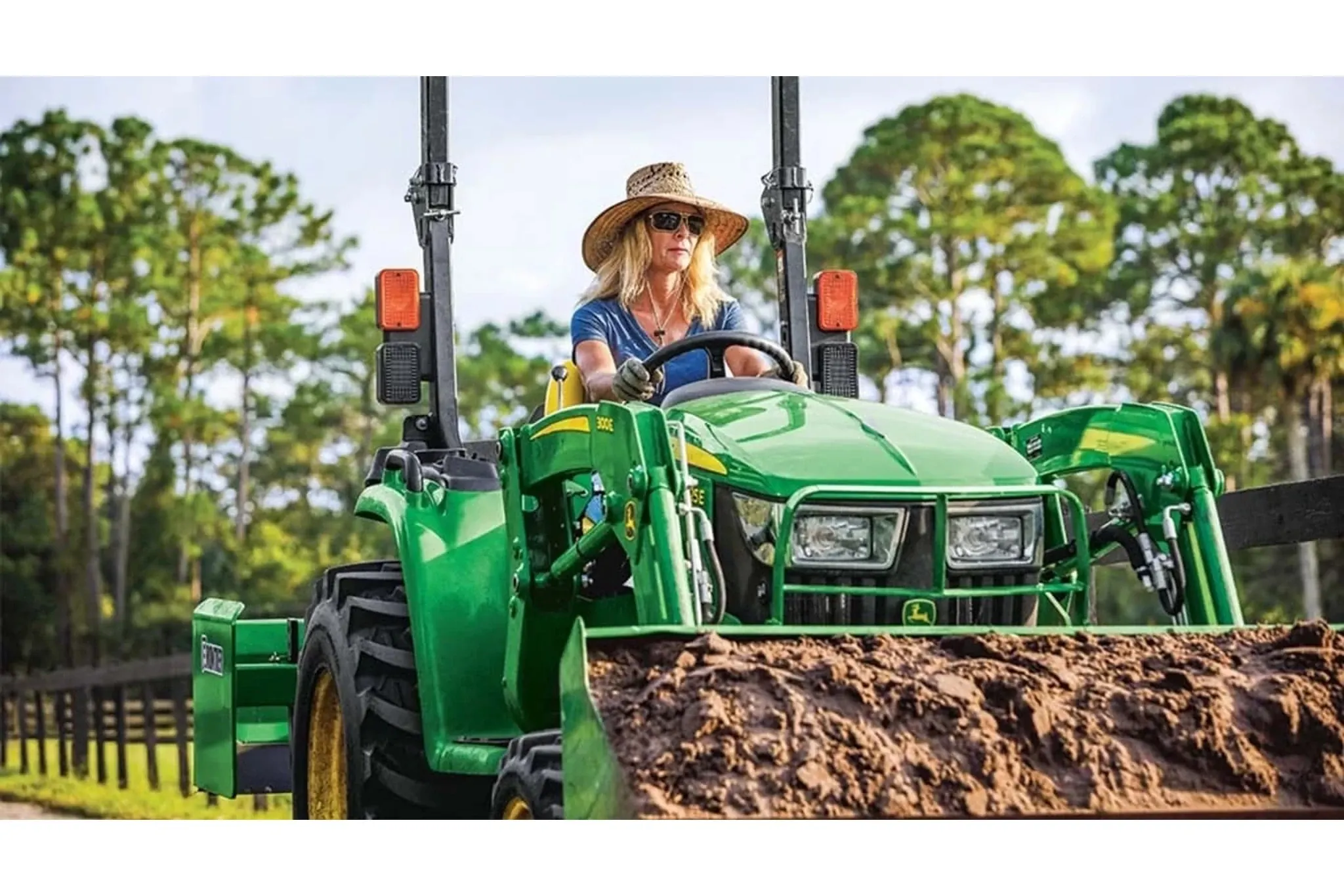 3025E 3 Series Compact Tractors with an operator driving a tractor in a field with a large pile of dirt