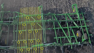 Top-down view of a field cultivator in a field, with yellow overlay lines and circles highlighting spacing points across the working width of the machine