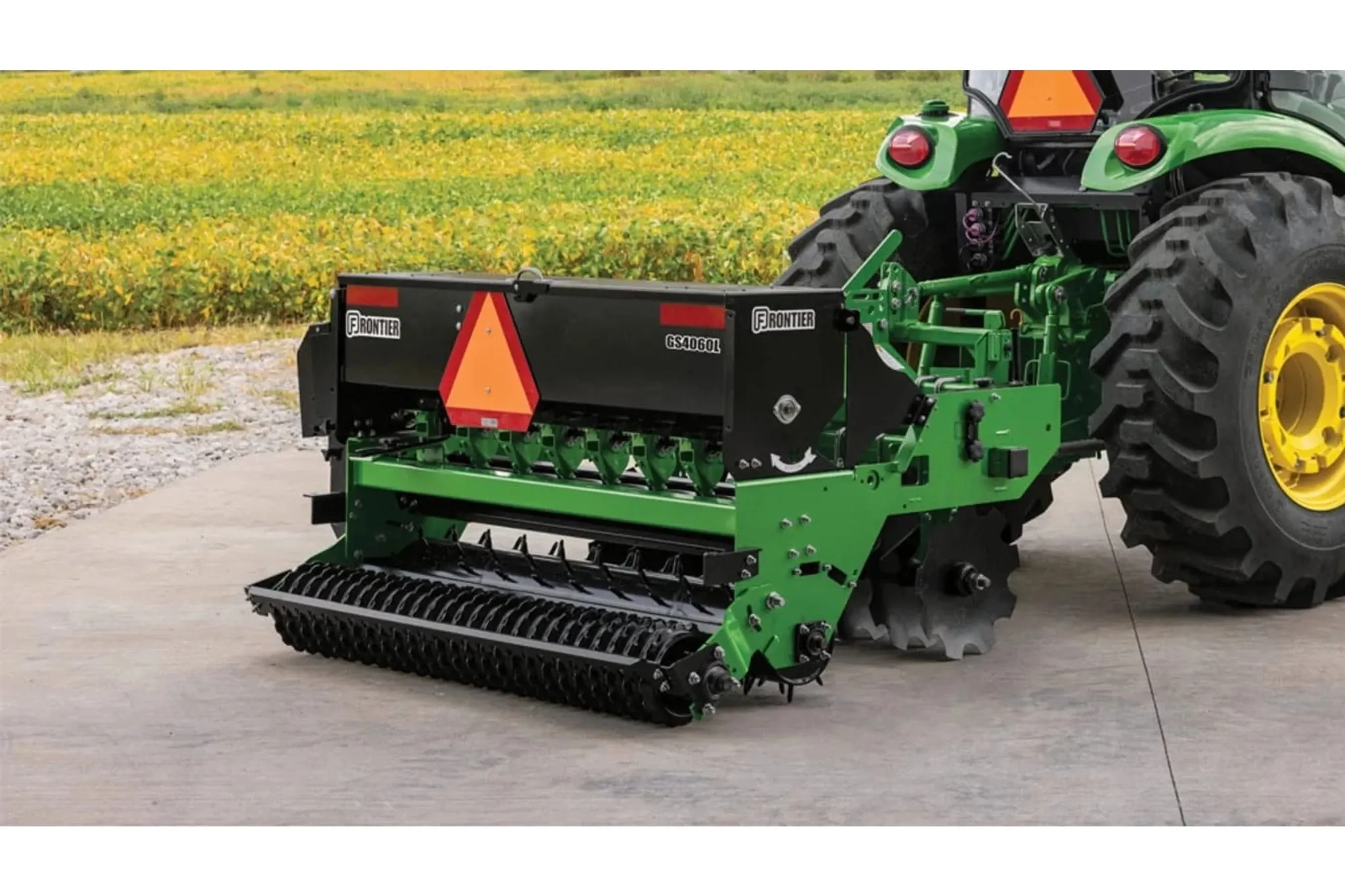 Right rear view of Frontier GS4060L ground seeder hooked up to a tractor next to a field