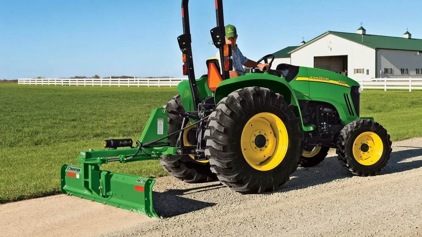 Farmer driving a tractor with a Frontier RB21H rear blade down a dirt road