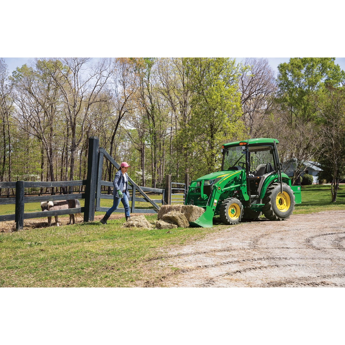 Green 320R tractor parked alongside a horse pen, with driver walking toward it to pick up hay bales in its front loader bucket Green 320R tractor parked alongside a horse pen, with driver walking toward it to pick up hay bales in its front loader bucket