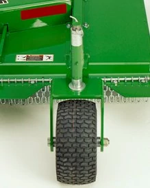Rear view of a green grooming mower implement showing a single treaded support wheel, adjustment post, and chain curtain