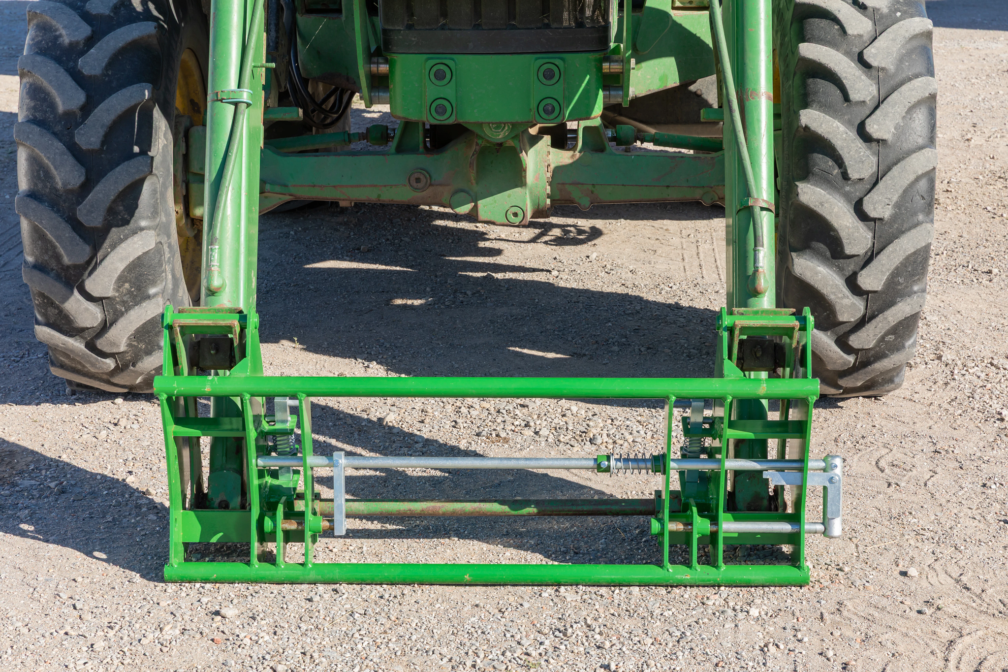 Rear view of a green tractor showing a mounted implement frame spanning between the rear wheels, with metal linkage arms and adjustment rods.