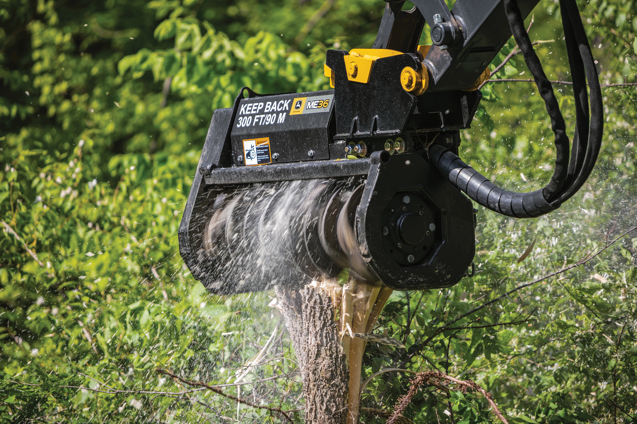 Forestry mulcher attachment mounted on a heavy machine cutting into a tree trunk, with wood chips and debris spraying outward