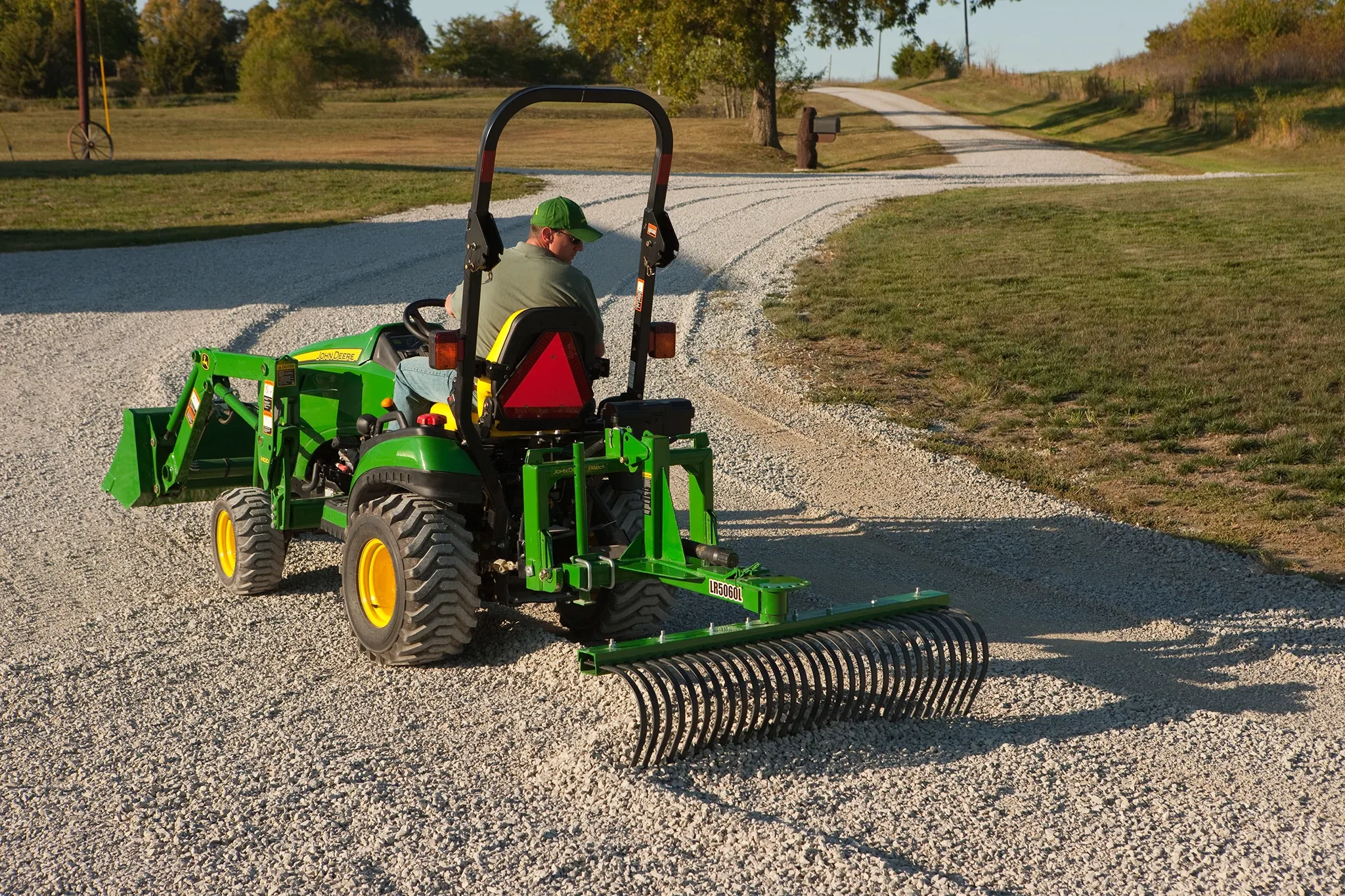 Man drives tractor pulling a landscape rake on a road