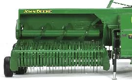 Front studio view of a small square baler's full-width feeding pickup machinery: teeth near the ground with an auger above.