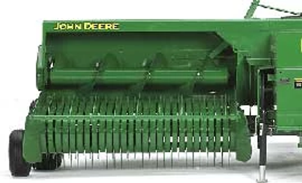 Front studio view of a small square baler's full-width feeding pickup machinery: teeth near the ground with an auger above.