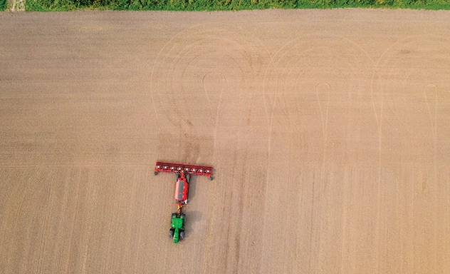 Aerial view of tractor pulling seed drill across field, showing precision seeding patterns and efficient field coverage.