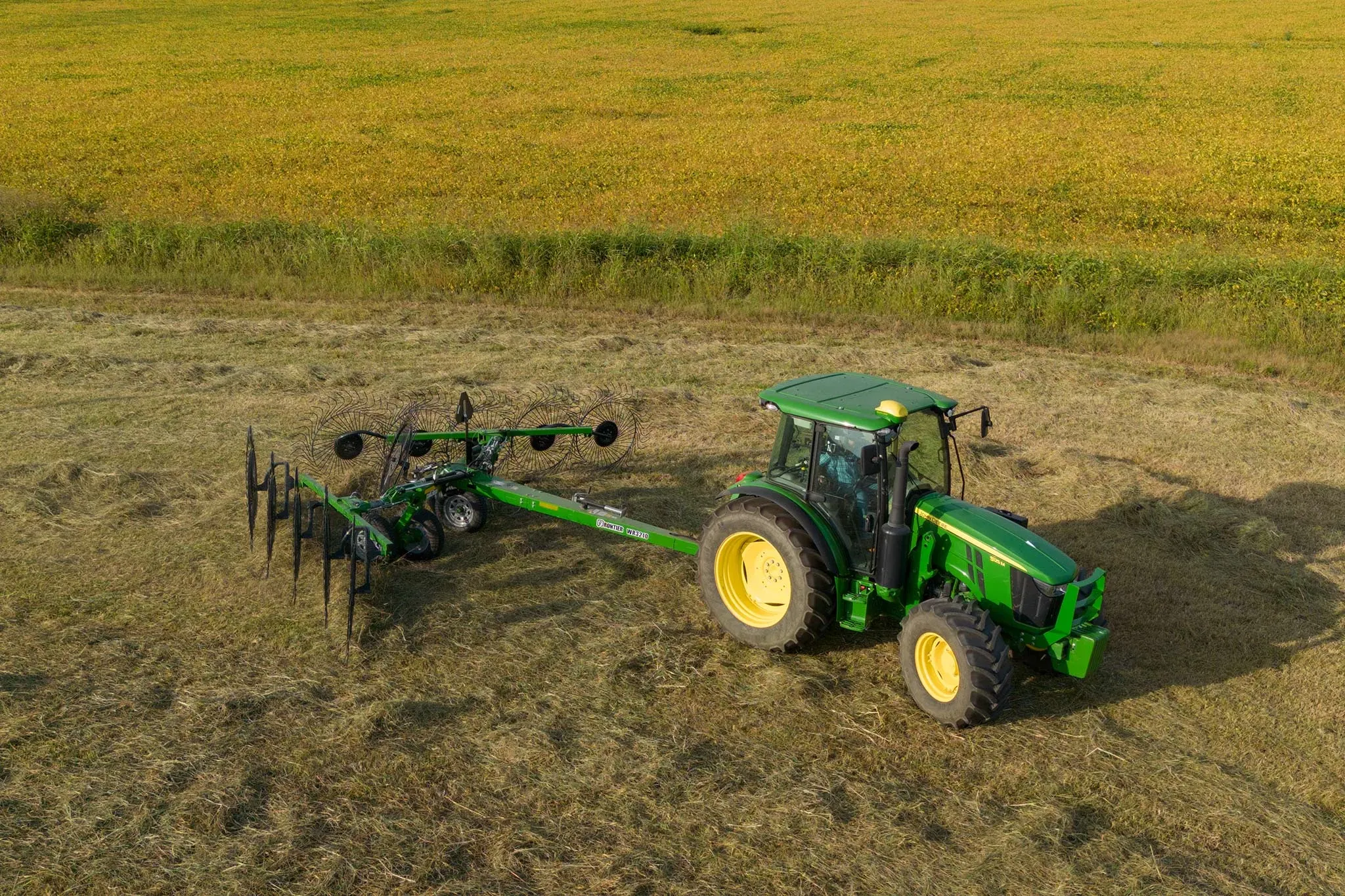 Top right view of a 5125M tractor pulling a WR3210 wheel rake across a swatch of felled hay