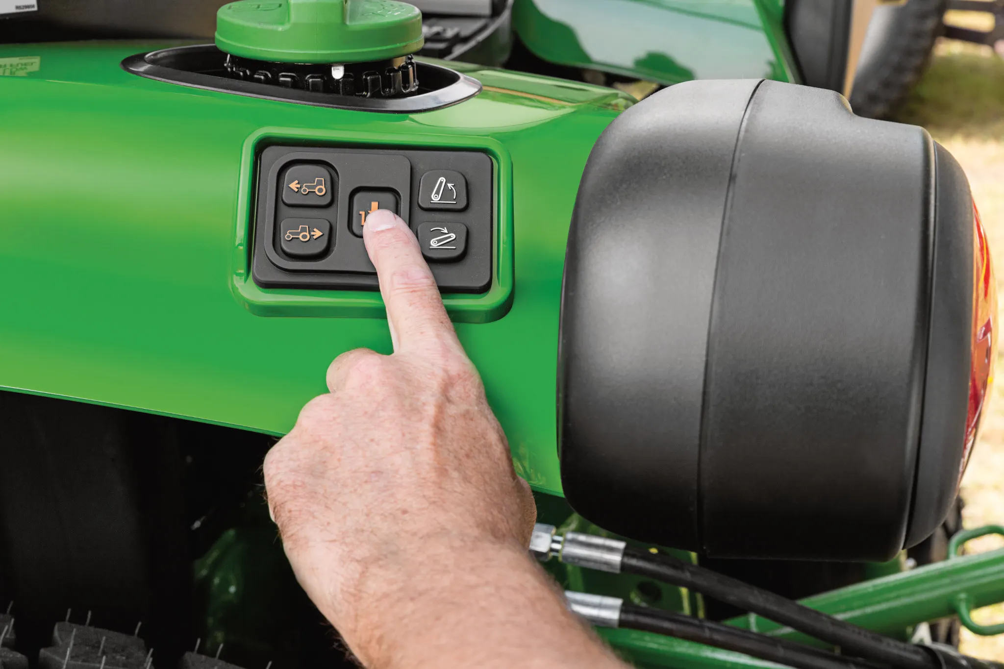 Image of someone pressing the hitch assist on a compact tractor