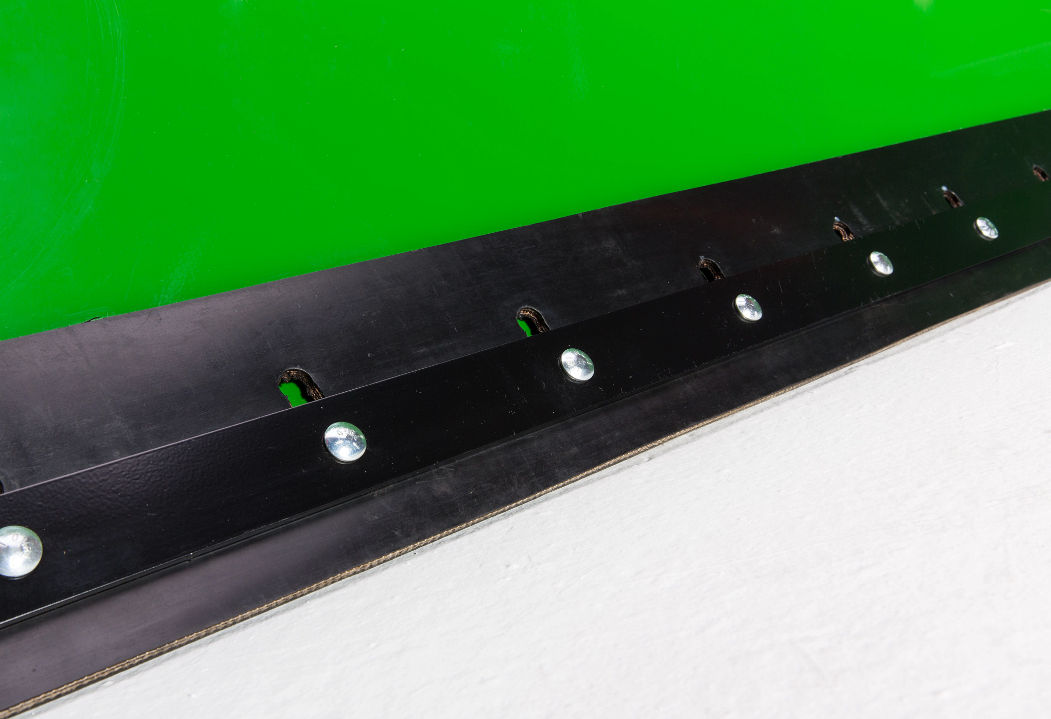 Close-up of a machine edge with a black reinforced cutting strip secured by evenly spaced silver bolts.