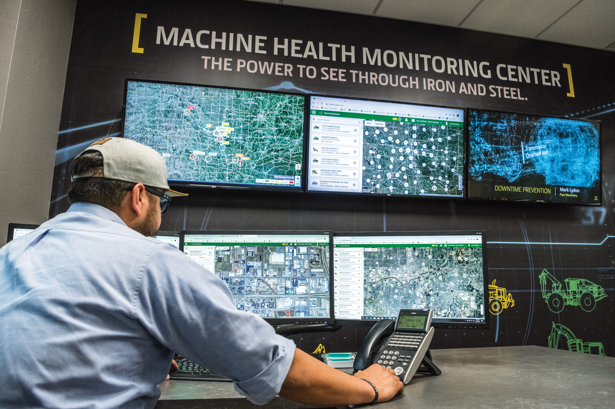 Man seated at a workstation looking at multiple large screens displaying equipment maps, diagnostics data, and system interfaces on the wall