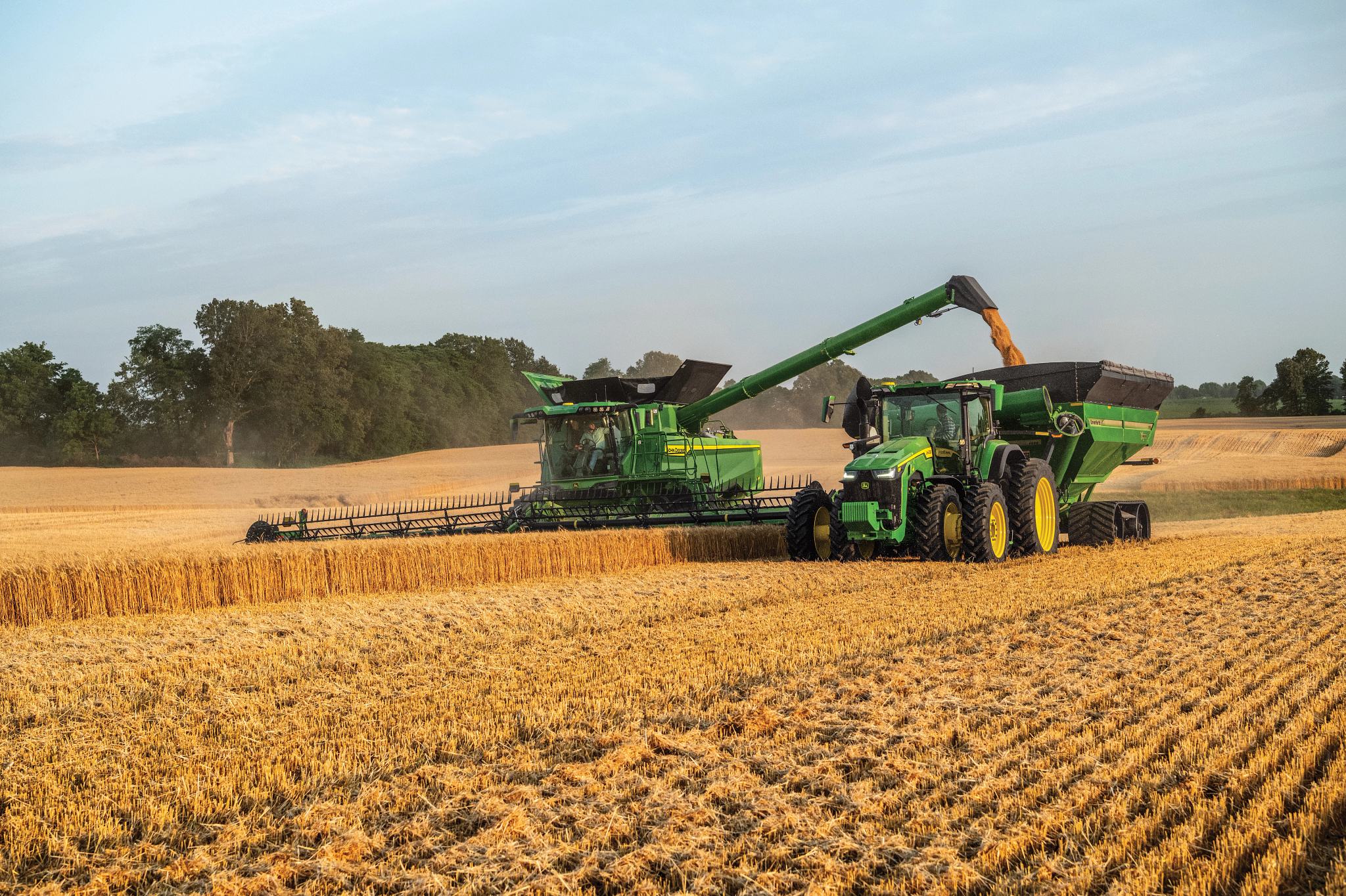 John Deere combine unloading into a grain cart during harvest — Koenig Equipment