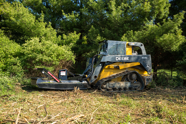 333E Compact Track Loader with an RS72 Rotary Cutter clearing brush along a tree line