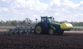 Side right view of a tractor in dirt field completing a field pass with Active Implement Guidance (AIG)