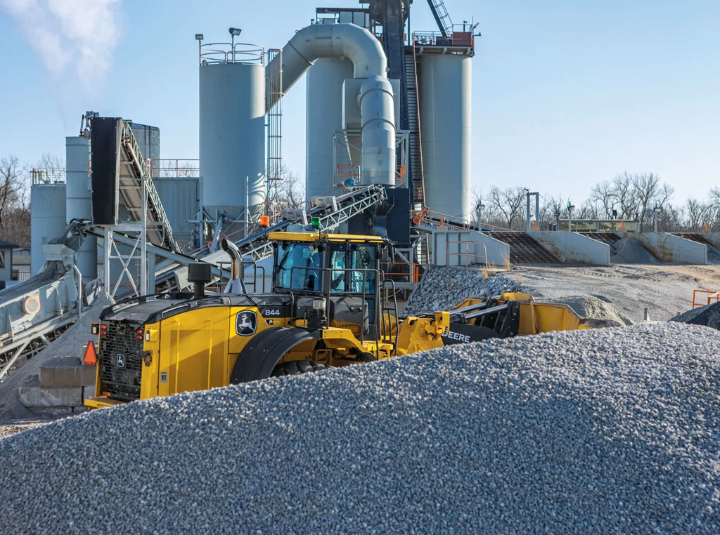 A Wirtgen W220Fi cold milling machine working in front of a large factory building