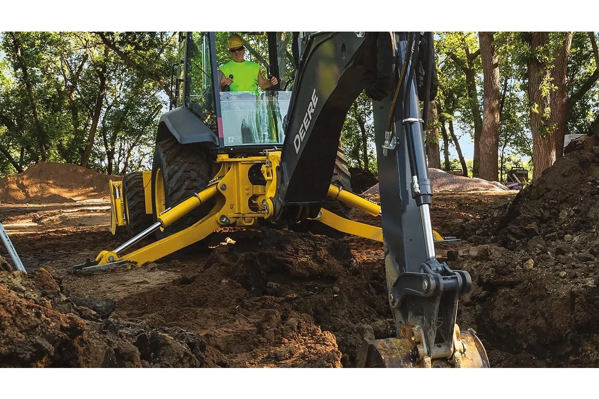 An operator digging a hole in a wooded area with a 710 P-Tier Backhoe