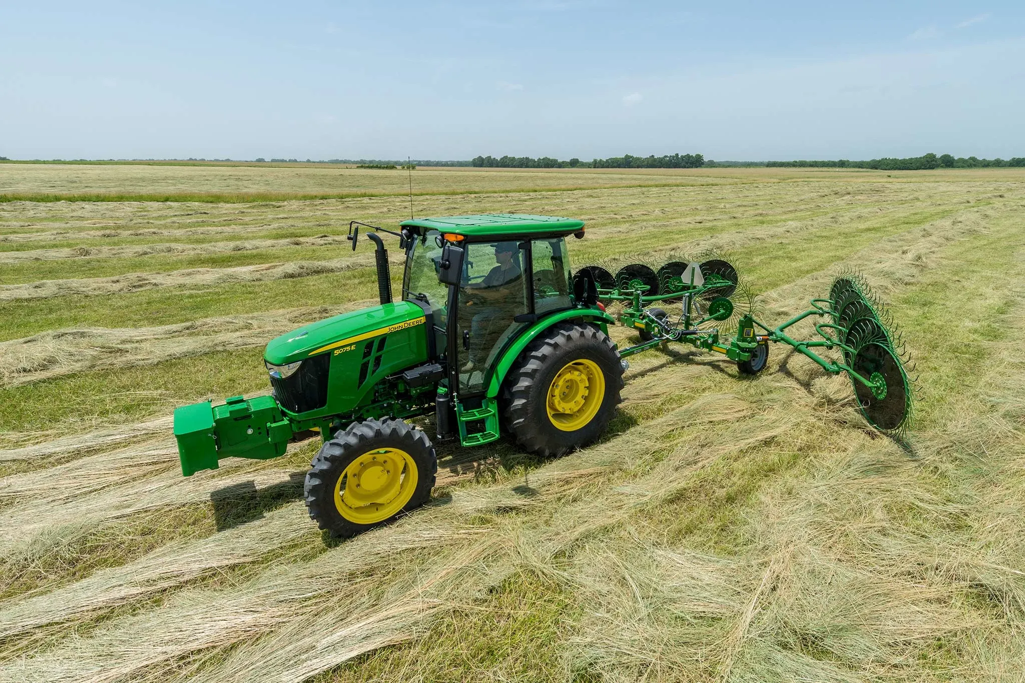 Side left view of a 5075E tractor with attached WR00 series wheel rake at work in a hay field