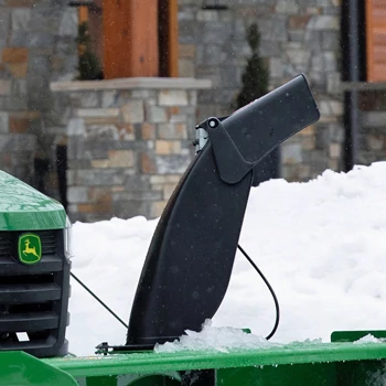 Close-up of a snow blower showing the black discharge chute rising from the housing, with snow buildup on the machine.