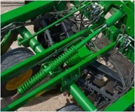 Close‑up of a green folding disk frame showing springs, hydraulic lines, and structural components above the wheels