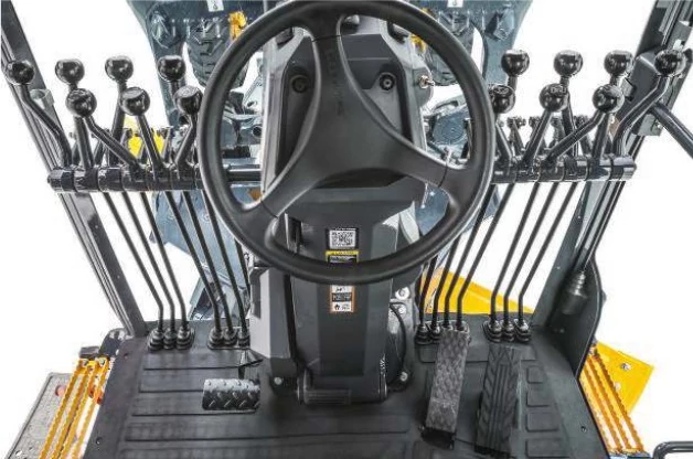 View inside G-Tier motor grader cab showing steering wheel and lever controls on forward rack
