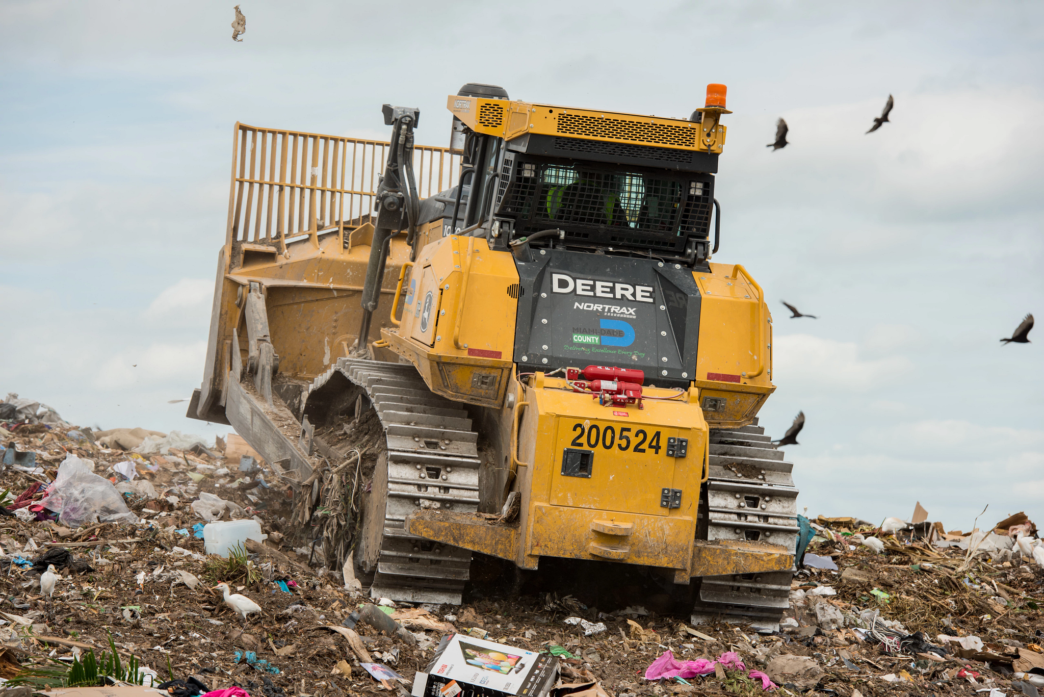 Tracked dozer operating at a landfill, pushing debris and waste uphill with a front blade.