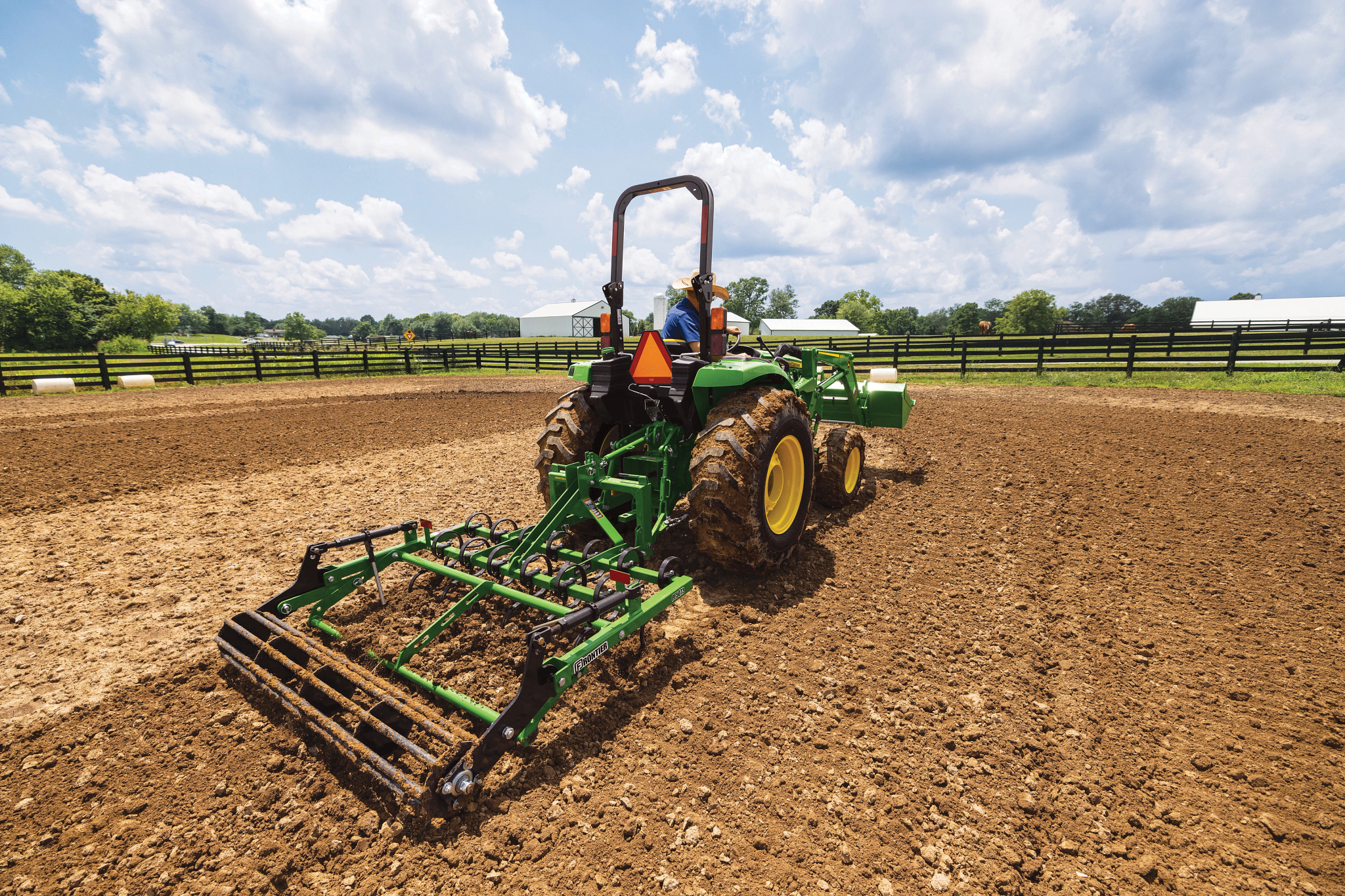 Rear right view of a tractor pulling a PF5072 pro finisher across an outdoor horse corral