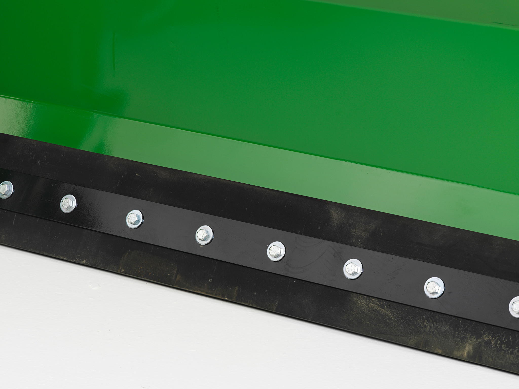 Close-up of the lower edge of a snow push blade showing a rubber cutting edge secured with evenly spaced bolts