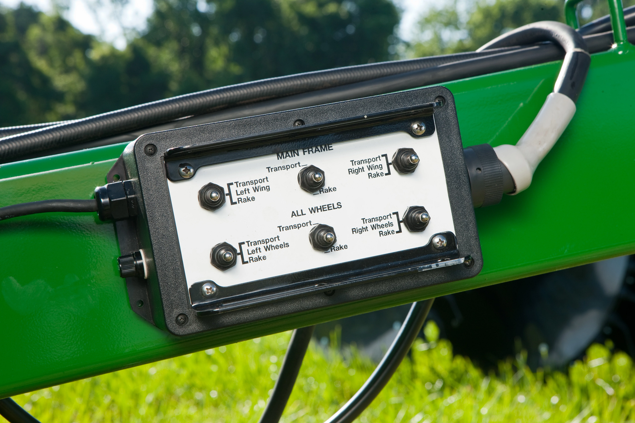 Close-up of the master control switch box on a wheel rake, mounted on a green bar amidst three cables.