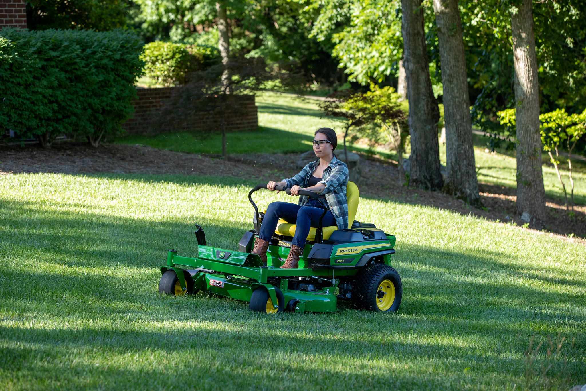 Front left view of an operator driving a Z315E ZTrak zero-turn mower with 42-in. mower deck across a shady lot