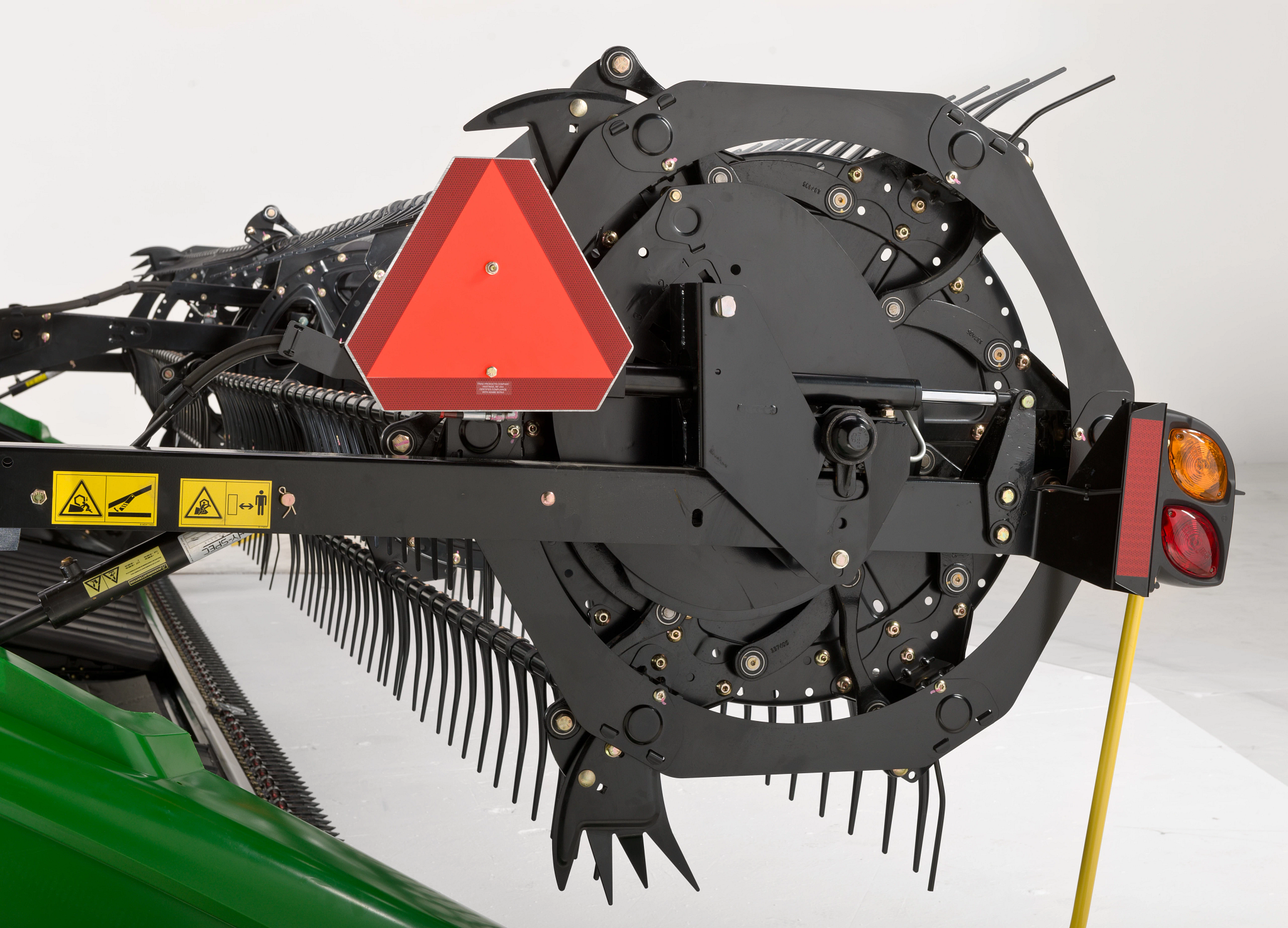 Close-up of the end of a windrower header, showing the circular drive mechanism, reel arms with tines, and safety and lighting components