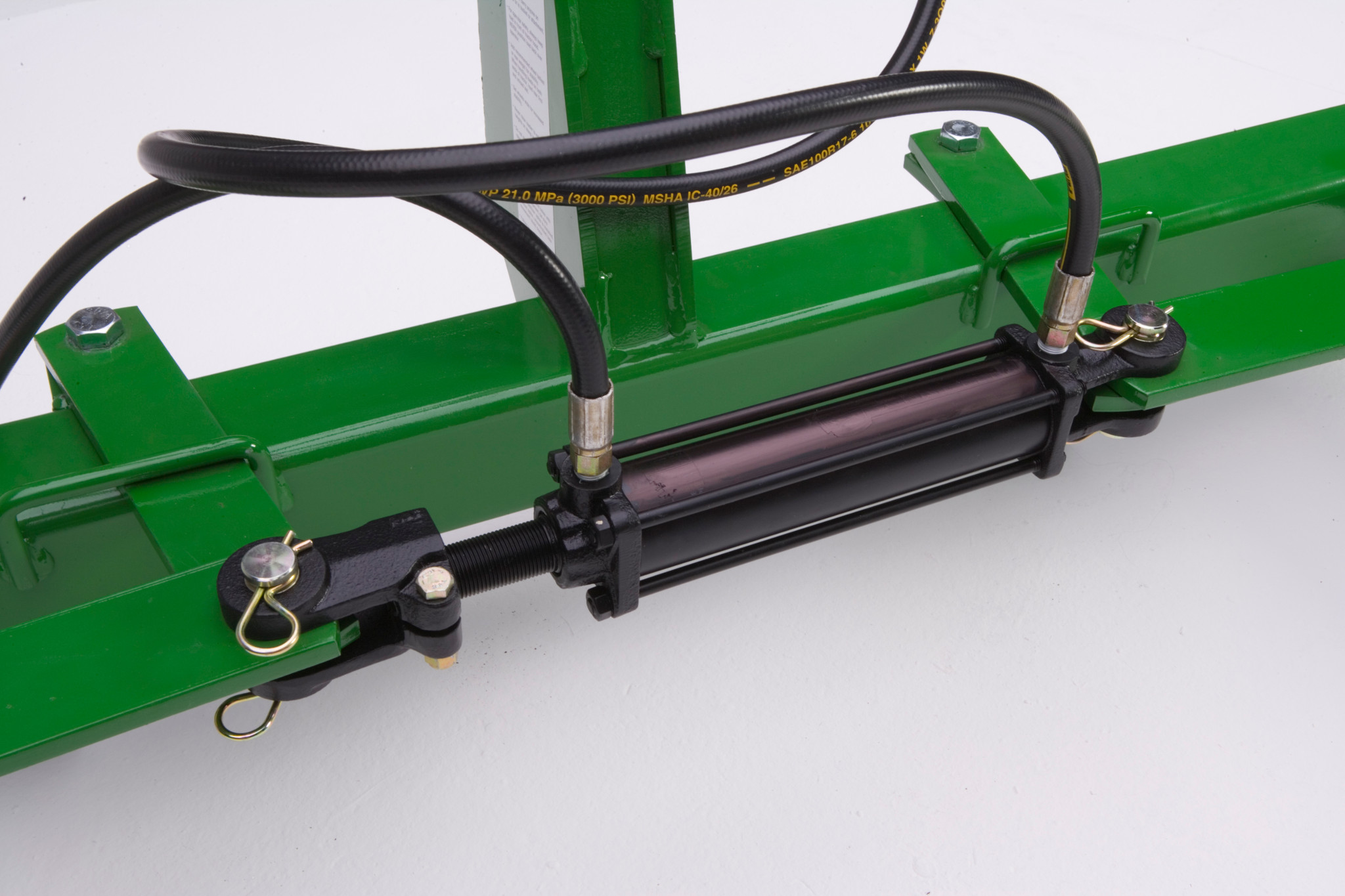 Close-up of a hydraulic cylinder mounted on a green bale unroller frame with two attached hydraulic hoses