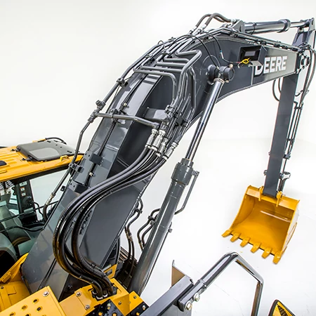 Close-up of an excavator boom and arm assembly with hydraulic hoses and metal lines along the dark gray boom, leading to the yellow digging bucket at the end