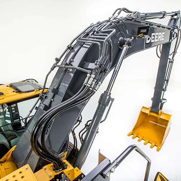 Close-up of an excavator boom and arm assembly with hydraulic hoses and metal lines along the dark gray boom, leading to the yellow digging bucket at the end