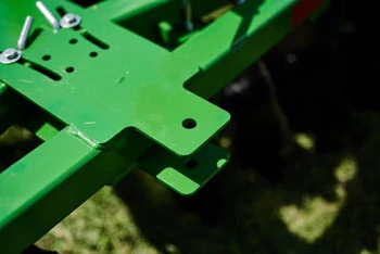 Close‑up of a green agricultural frame showing a flat metal mounting plate with bolt holes and fasteners.